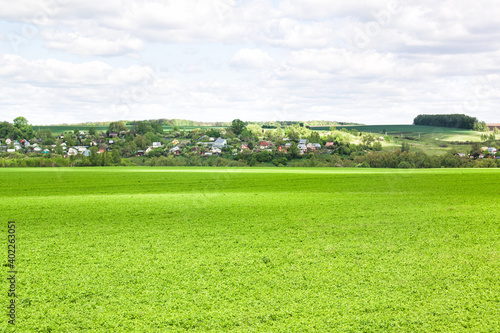 A lawn with green grass all the way to the horizon. Horizontal landscape of a flat field with fresh spring grass. Village, country houses, SNT, on the background of fields and trees. photo