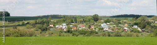 A lawn with green grass all the way to the horizon. Horizontal landscape of a flat field with fresh spring grass. Village, country houses, SNT, on the background of fields and trees.