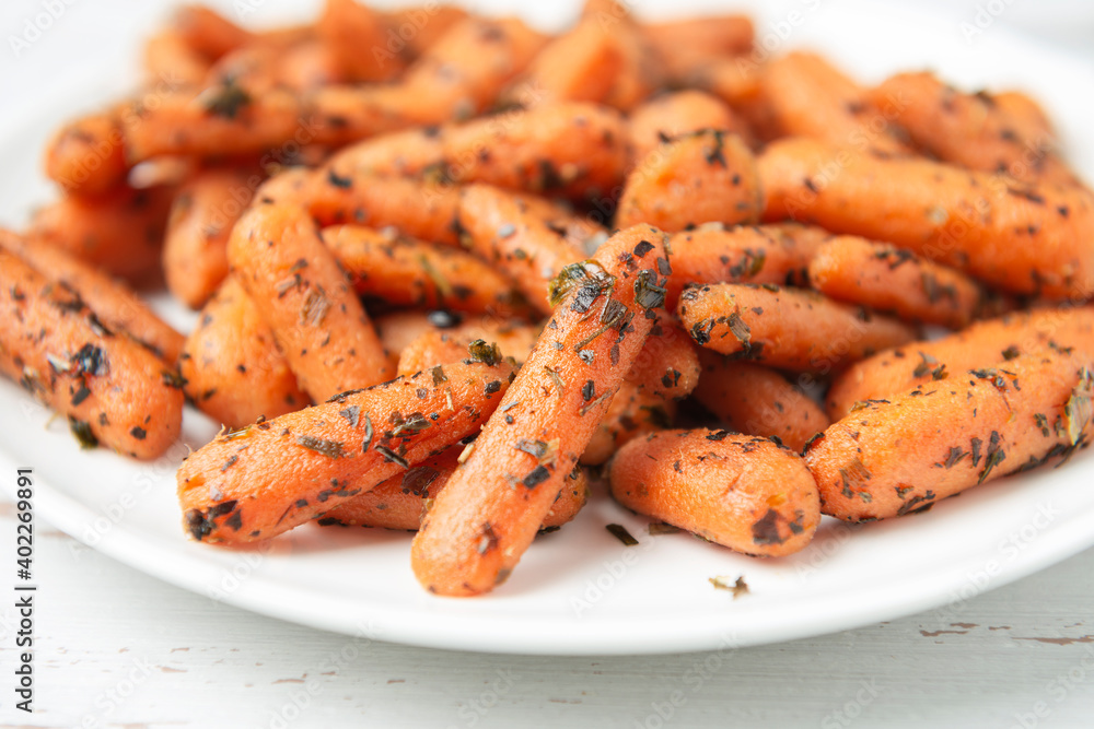 White plate with small peeled pieces of cooked baby carrot on white textured wooden table White plate with small peeled pieces of cooked baby carrot on white textured wooden table
