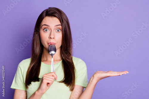 Photo portrait of young girl licking spoon staring keeping empty space on hands isolated on vivid purple color background