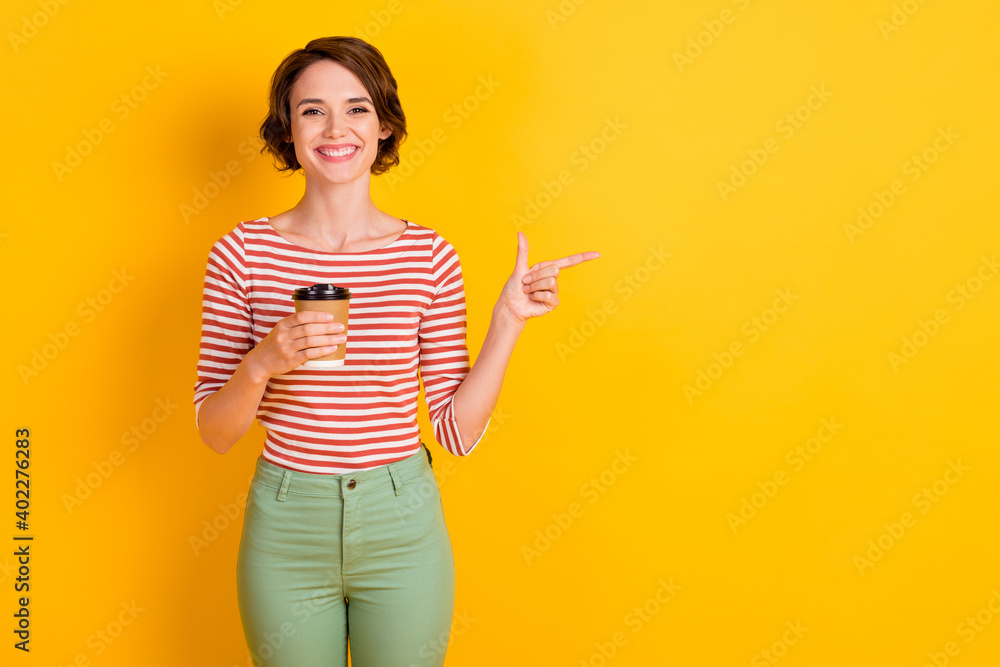 Portrait of attractive positive lady hold beverage finger indicate empty space isolated on yellow color background Portrait of attractive positive lady hold beverage finger indicate empty space isolated on yellow color background