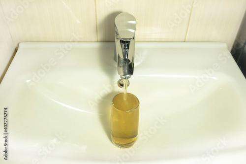 Dirty tap water flows out of the mixer. A glass cup filled with muddy water is in the sink.