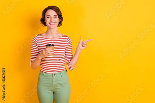 Portrait of attractive positive lady hold beverage finger indicate empty space isolated on yellow color background