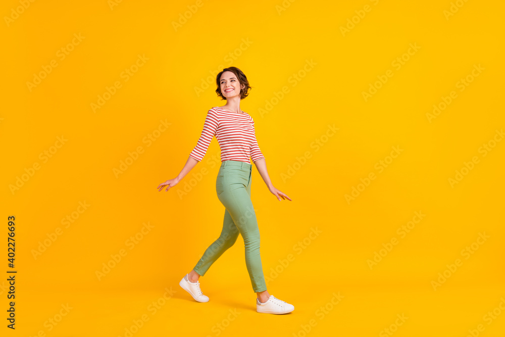 Full length photo of charming shiny woman wear striped outfit walking looking back empty space isolated pink color background