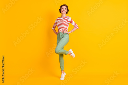 Full length body size photo of cheerful girl smiling standing tiptoes isolated on vibrant yellow color background