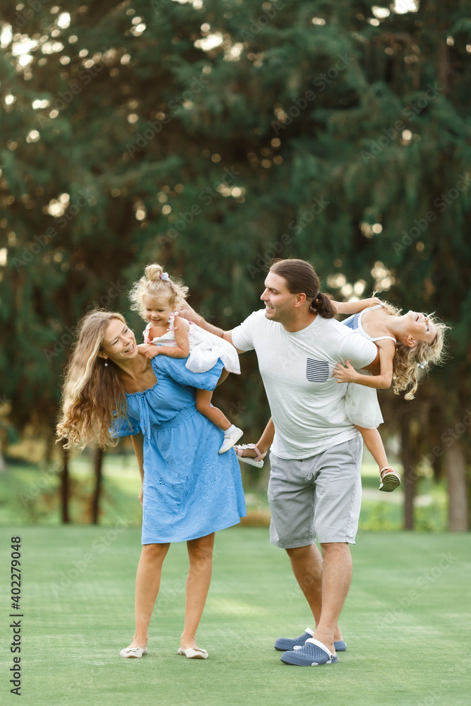 Fototapeta premium Parents Giving Children Piggybacks In Countryside, enjoing time together. Happy family concept. Blurred trees background.