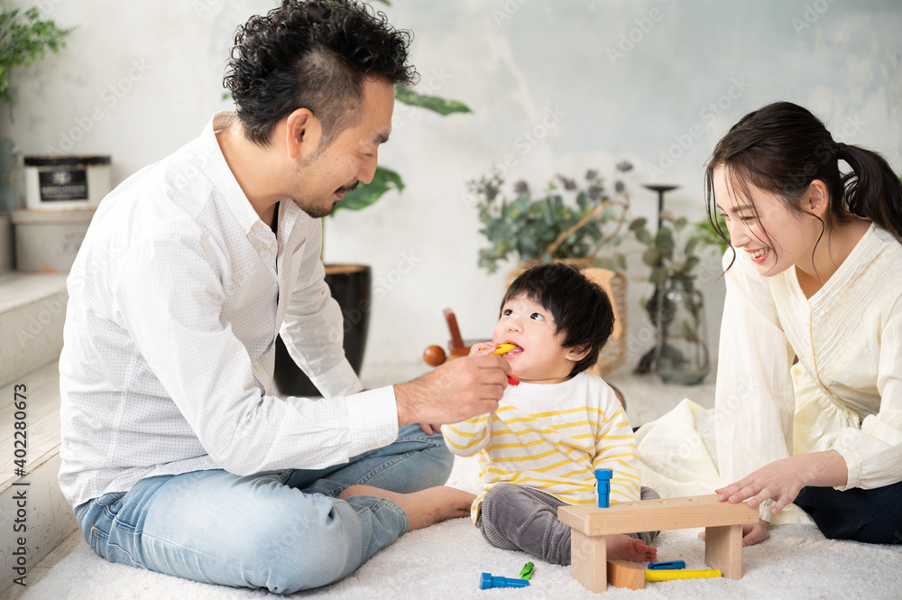 Obraz premium 新築の様な白くて広い部屋でイケメンの旦那さんが赤ちゃんをあやす家族団らんの幸せな若いファミリー