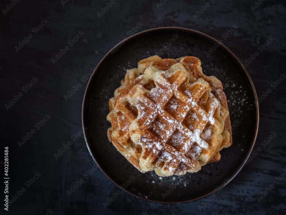 Homemade waffles with powdered sugar on a round black plate