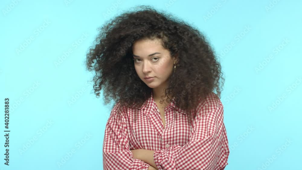 Slow motion of moody girlfriend with long curly hair, looking upset and offended, cross arms on chest and turn away, sulking at boyfriend, unwilling to talk, standing over turquoise background
