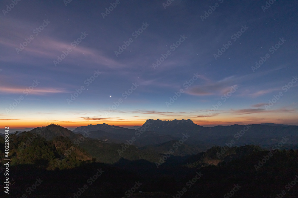 Early morning view mountain pass, with visible multitude of stars on the sky above the mountains. Sun is slowly  to rise and glow is visible.