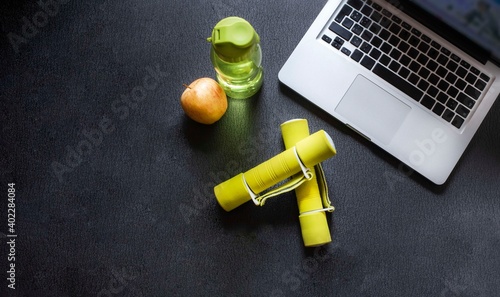 laptop, dumbbells, bottle of water and apple. Exercise at home, healthy life concept. Image with copy space