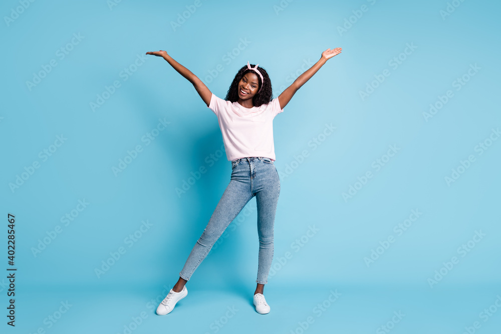 Obraz premium Full length photo of adorable pretty afro woman wear pink t-shirt denim hands arms up isolated blue color background