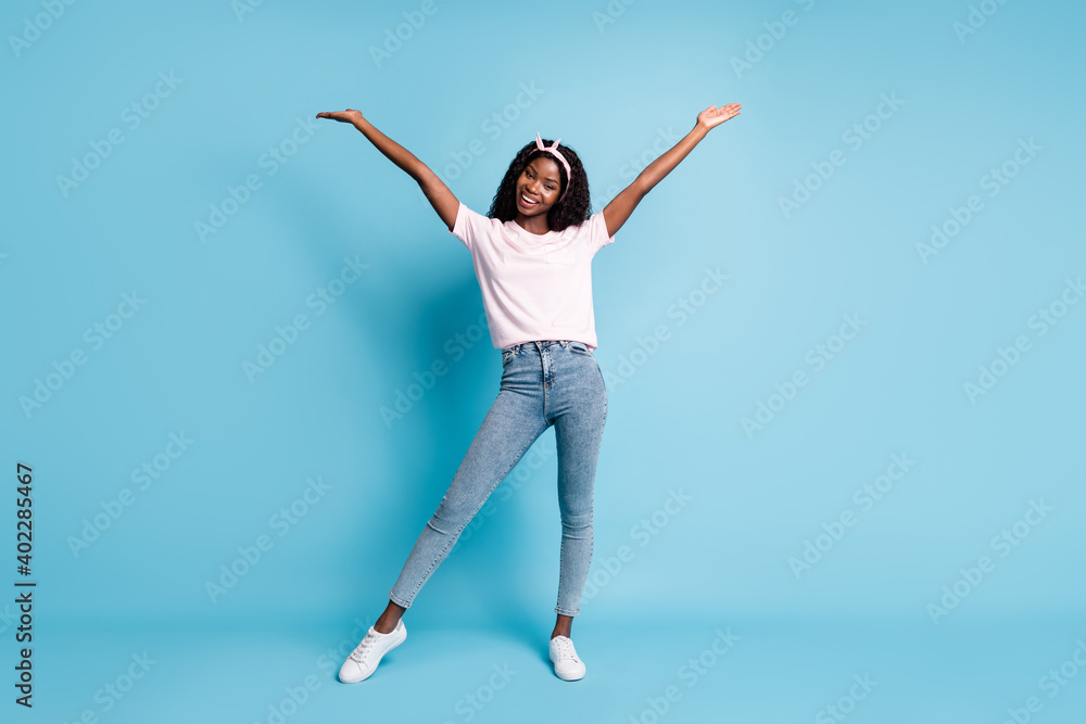 Full length photo of adorable pretty afro woman wear pink t-shirt denim hands arms up isolated blue color background