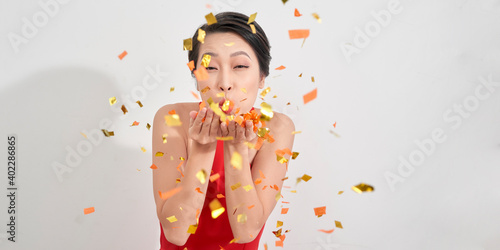 Happy smiling woman in amazing red dress celebrating new year party, blowing colorful confetti.