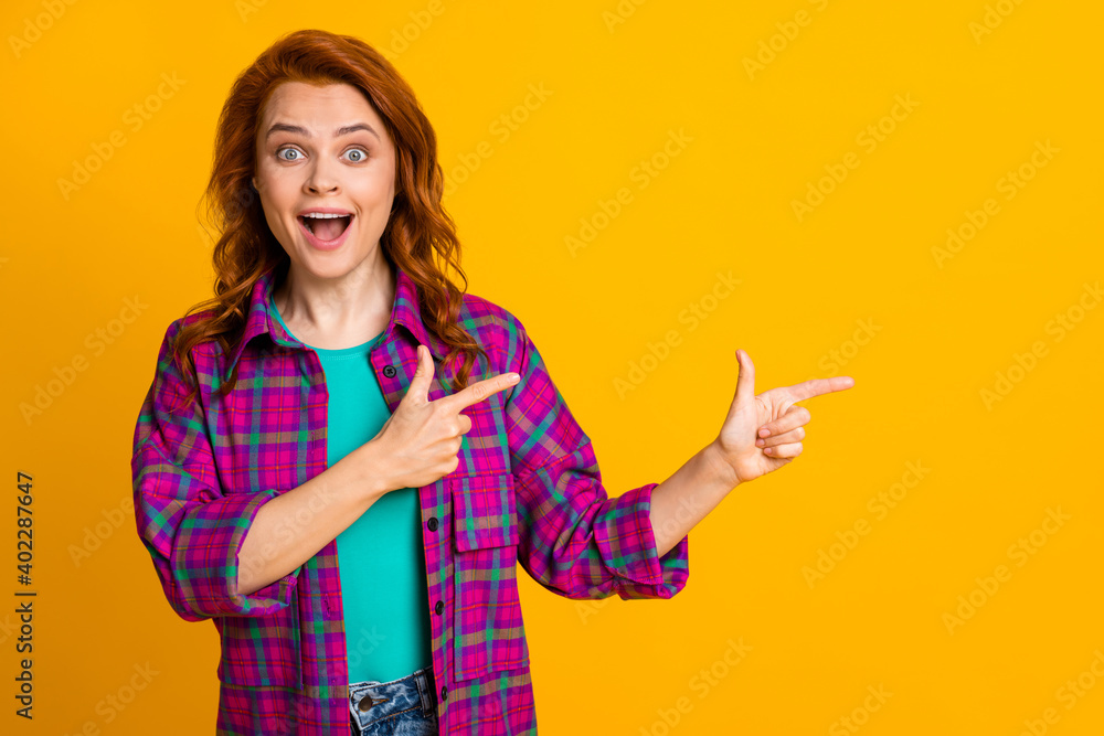 Portrait of impressed lady indicate fingers empty space open mouth wear checkered isolated on yellow color background Portrait of impressed lady indicate fingers empty space open mouth wear checkered isolated on yellow color background