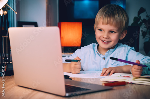 School boy with laptop at table in evening at home.