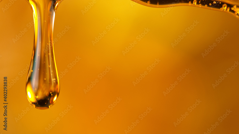 Pouring oil or honey drop on golden background. Macro shot.