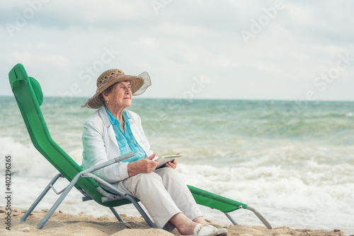  old woman 84 years old sitting on the seashore with a tablet computer in her hands. © Ann Stryzhekin