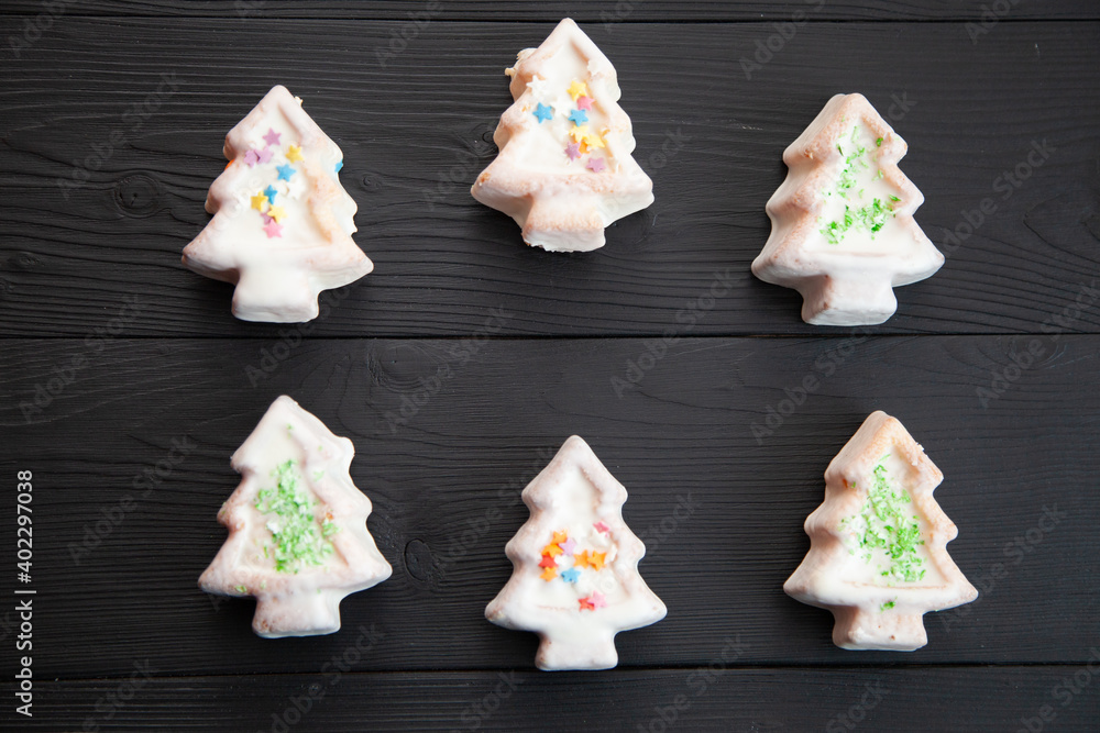 Christmas cookies in white glaze in the form of Christmas trees on a dark wooden background.