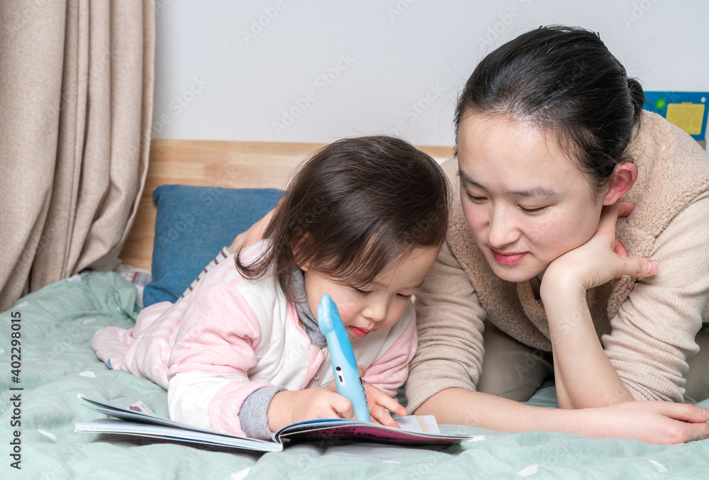 Mother and daughter sit on the bed reading together Mother and daughter sit on the bed reading together
