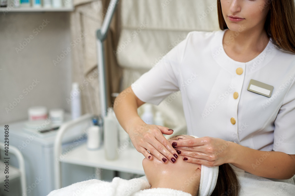 Obraz premium Hands of beautician making facial lifting massage for pretty young woman in SPA salon