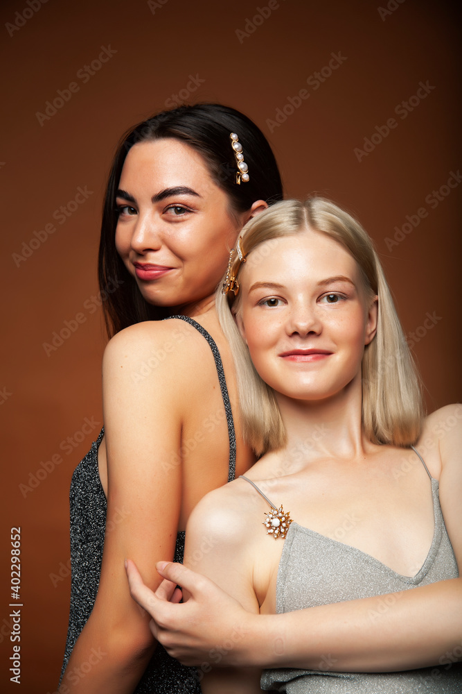 two pretty diverse girls happy posing together: blond and brunette on brown background, lifestyle people concept two pretty diverse girls happy posing together: blond and brunette on brown background, lifestyle people concept
