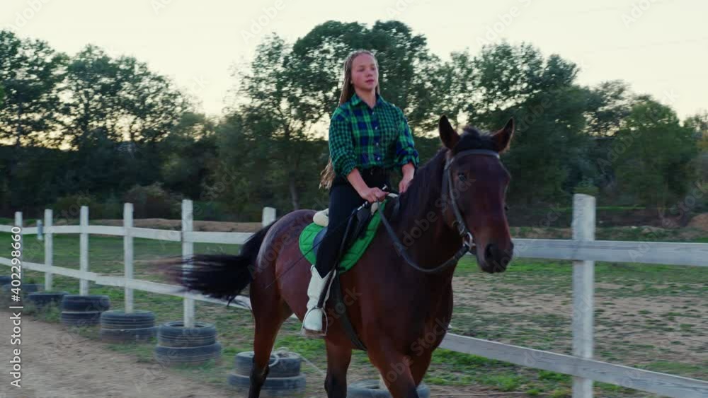 A teenage girl galloping on horseback at outdoor manege. A young girl riding a horse on the farm at dusk A teenage girl galloping on horseback at outdoor manege. A young girl riding a horse on the farm at dusk
