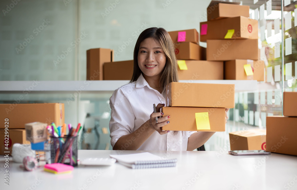 An Asian owner holds a package in a brown box, ready for delivery to a customer who orders online. As he sat in the home office An Asian owner holds a package in a brown box, ready for delivery to a customer who orders online. As he sat in the home office
