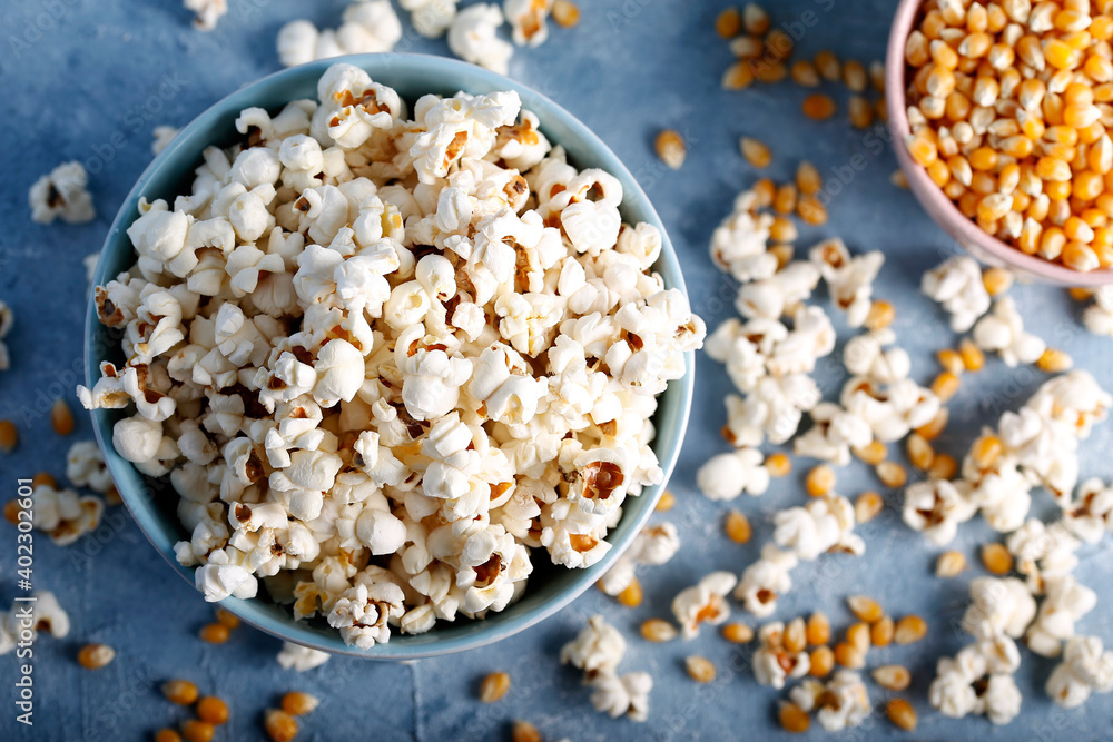 Salty popcorn in a blue bowl with corncobs on the blue background. Salty popcorn in a blue bowl with corncobs on the blue background.