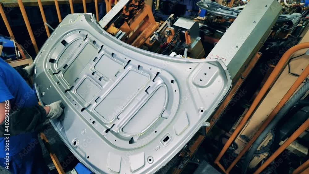 Car mechanic assembling a car hood at a car production factory Car mechanic assembling a car hood at a car production factory