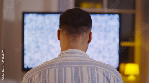 Back view of man sitting in front of tv with no signal