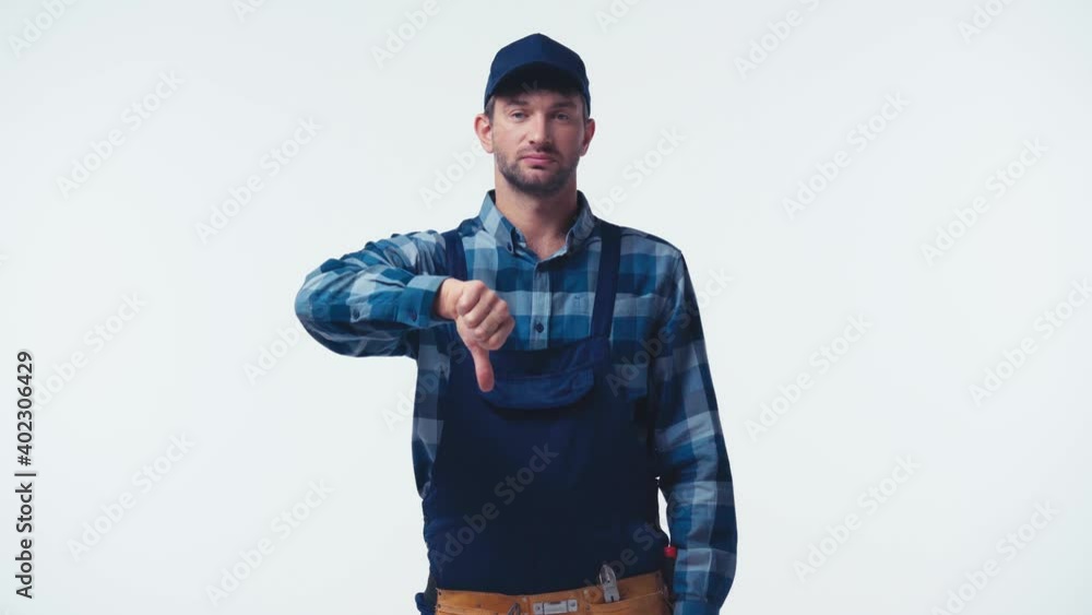 displeased handyman in uniform and cap showing thumb down isolated on white displeased handyman in uniform and cap showing thumb down isolated on white
