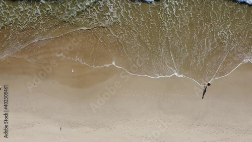 people walking along the beach in vertical drone view