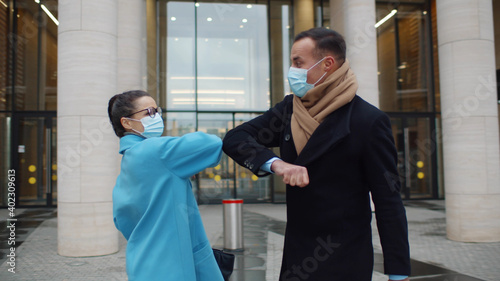 Business people in safety mask greeting with bumping elbows outdoors during covid-19 pandemic