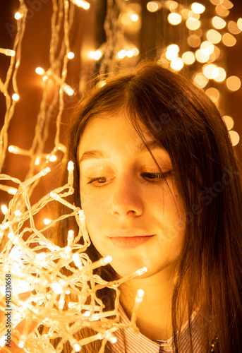 Portrait of a beautiful girl with a garland in her hands on a glowing background. © FO_DE