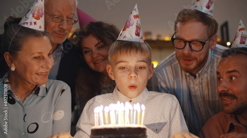 Cute boy blowing out birthday cake candles at family party photo