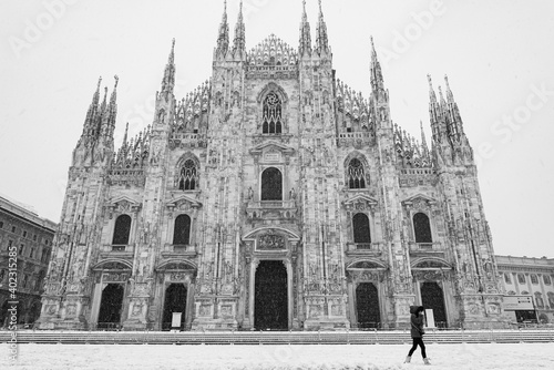 The facade of Milan cathedral (called Duomo) during a heavy snowfall with one person walking. Monochromatic