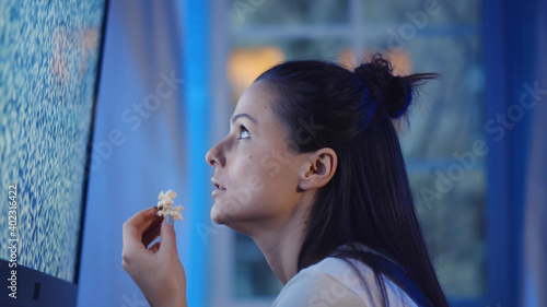 Side view of young woman eating popcorn and watching tv with noise on screen