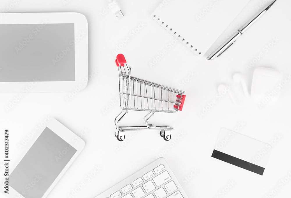 Shopping online concept. Small red trolley and gadgets on the table.