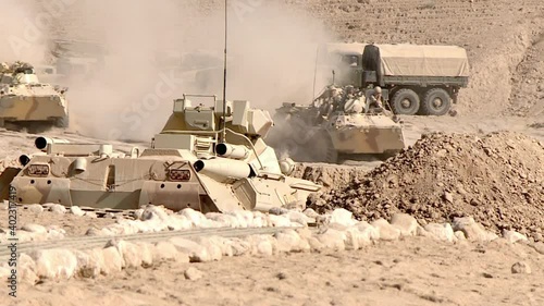 A column of armored military equipment leaves the location for a combat mission in the zone of military conflict, dust rises from under the wheels.