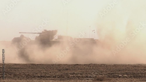An armored personnel carrier drives through the sand in the desert, raising a cloud of dust. Concept: war zone in the east, movement of military equipment.