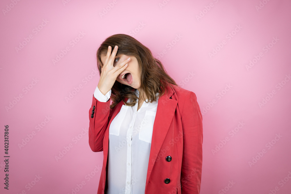 Young business woman over isolated pink background peeking in shock covering face and eyes with hand, looking through fingers with embarrassed expression Young business woman over isolated pink background peeking in shock covering face and eyes with hand, looking through fingers with embarrassed expression
