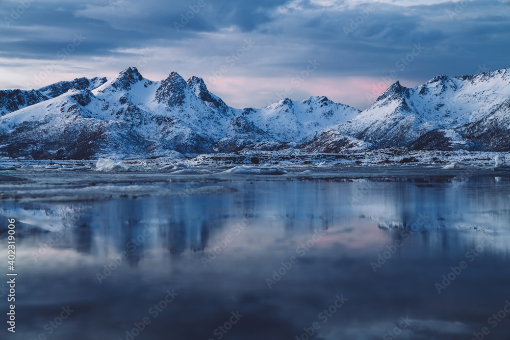 Cloudy sundown sky over snowy mountains located on shore of frozen sea