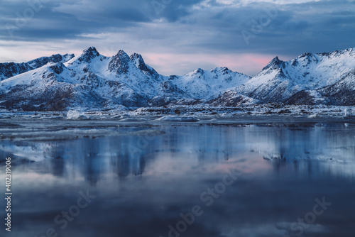 Cloudy sundown sky over snowy mountains located on shore of frozen sea