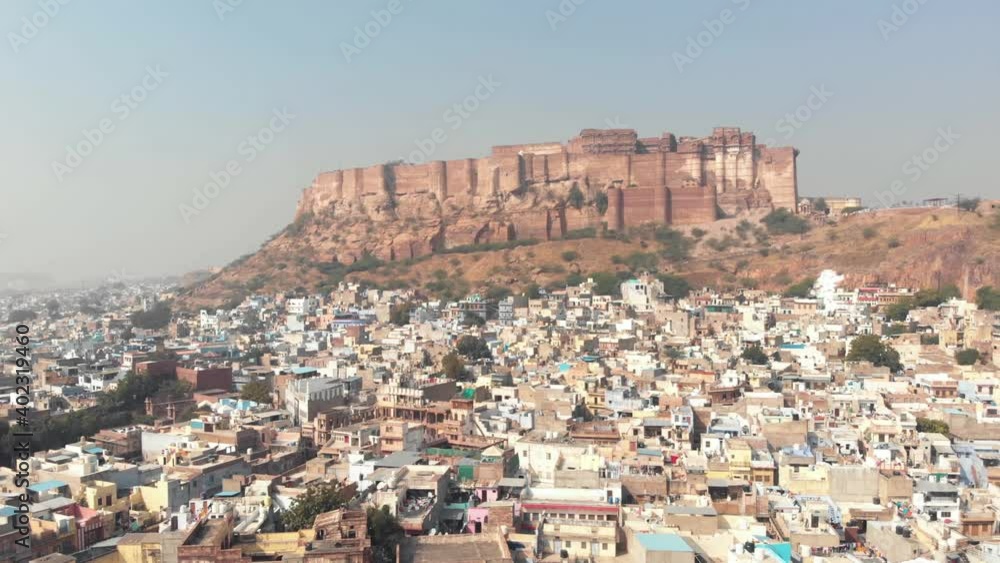 Blue City landscape of Jodhpur surrounding Mehrangarh Fort standing above cliff in Rajasthan, India - Aerial Pan Reveal shot Blue City landscape of Jodhpur surrounding Mehrangarh Fort standing above cliff in Rajasthan, India - Aerial Pan Reveal shot