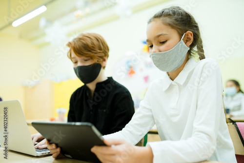 A girl and a boy during a pandemic study at school holding tablets in their hands