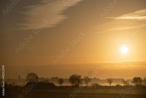 Sonnenaufgang über Feld und Dorf im Herbst/Winter mit Dunst