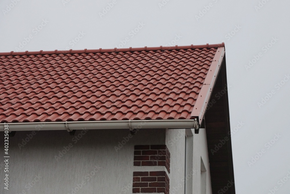 part of brown tiled roof and gray wall of a private house on the street against the background of the sky part of brown tiled roof and gray wall of a private house on the street against the background of the sky