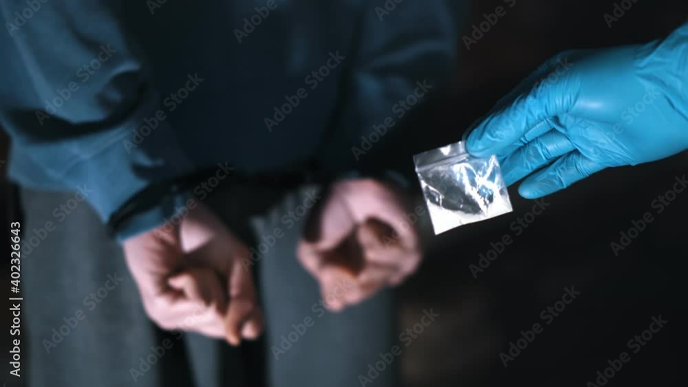 Close up of policeman in glove holding bag with crack and dealer in handcuffs Close up of policeman in glove holding bag with crack and dealer in handcuffs