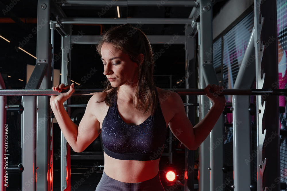 Beautiful young fitness woman doing squats with a barbell on the Smith Machine in the gym. Beautiful woman poses for the camera.
